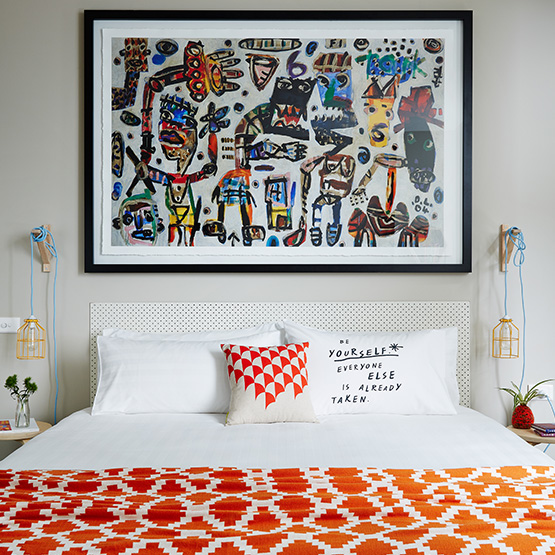 A hotel room with an orange patterned bed and an abstract painting